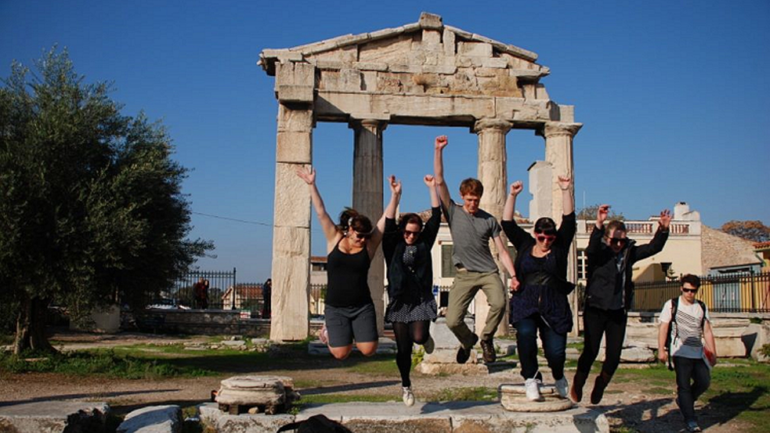 Greek Field Trip - students jump in the air outside of a monument.