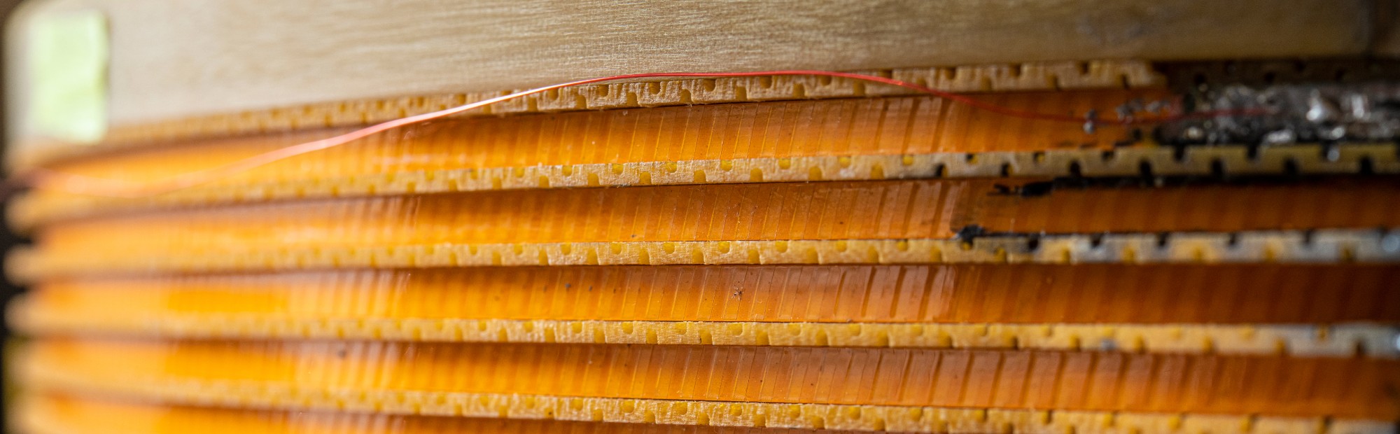 A thin red wire runs along a reel made of yellow and orange transformer coil