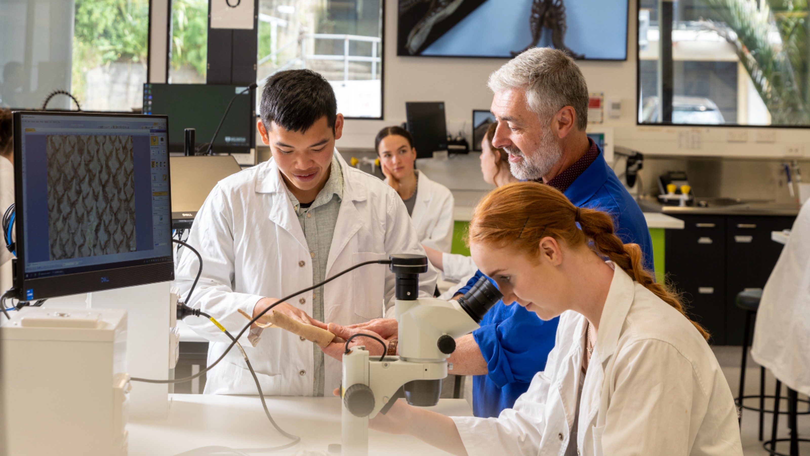 A group of students and a supervisor using a microscope in a lab