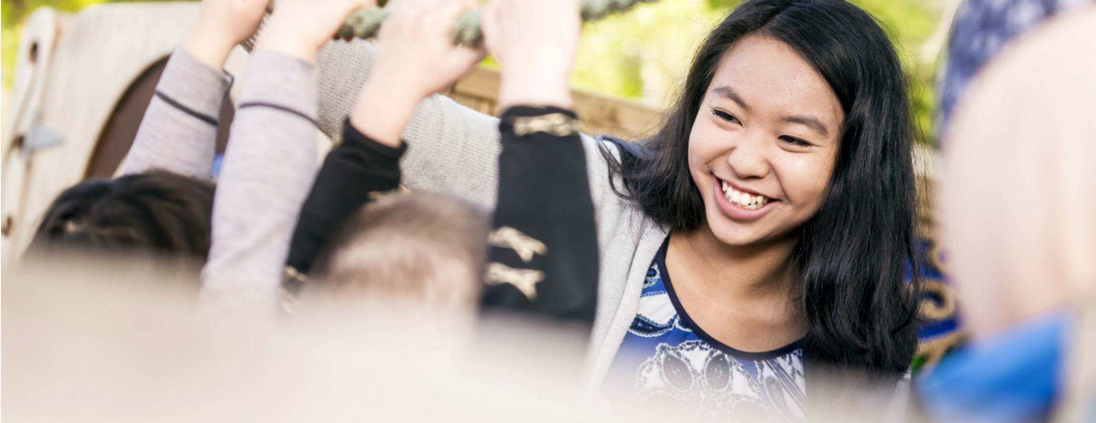 A woman smiles at children who are intently raising their hands.