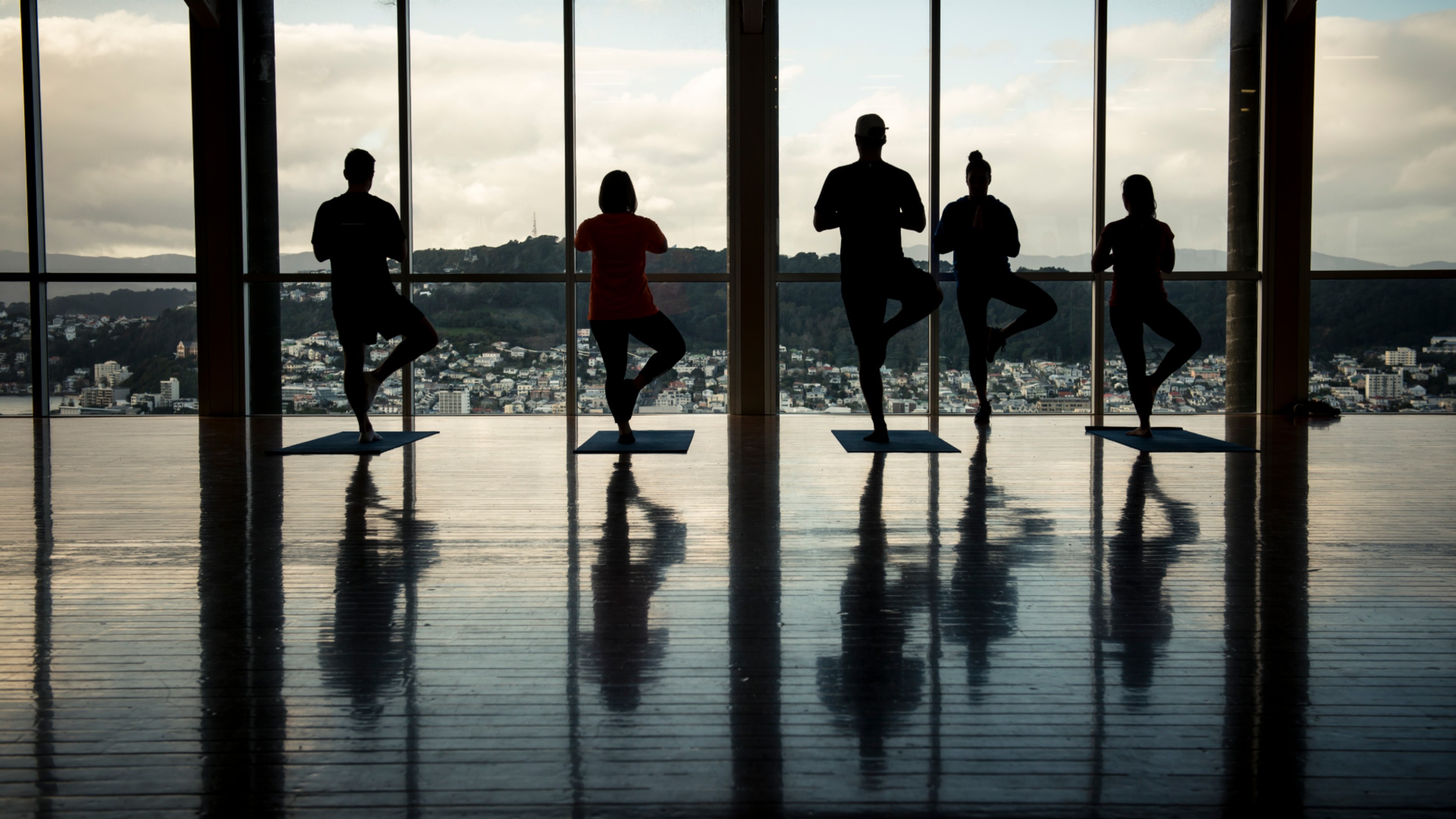 Five silhouttes standing on one leg in a yoga pose at sunset.