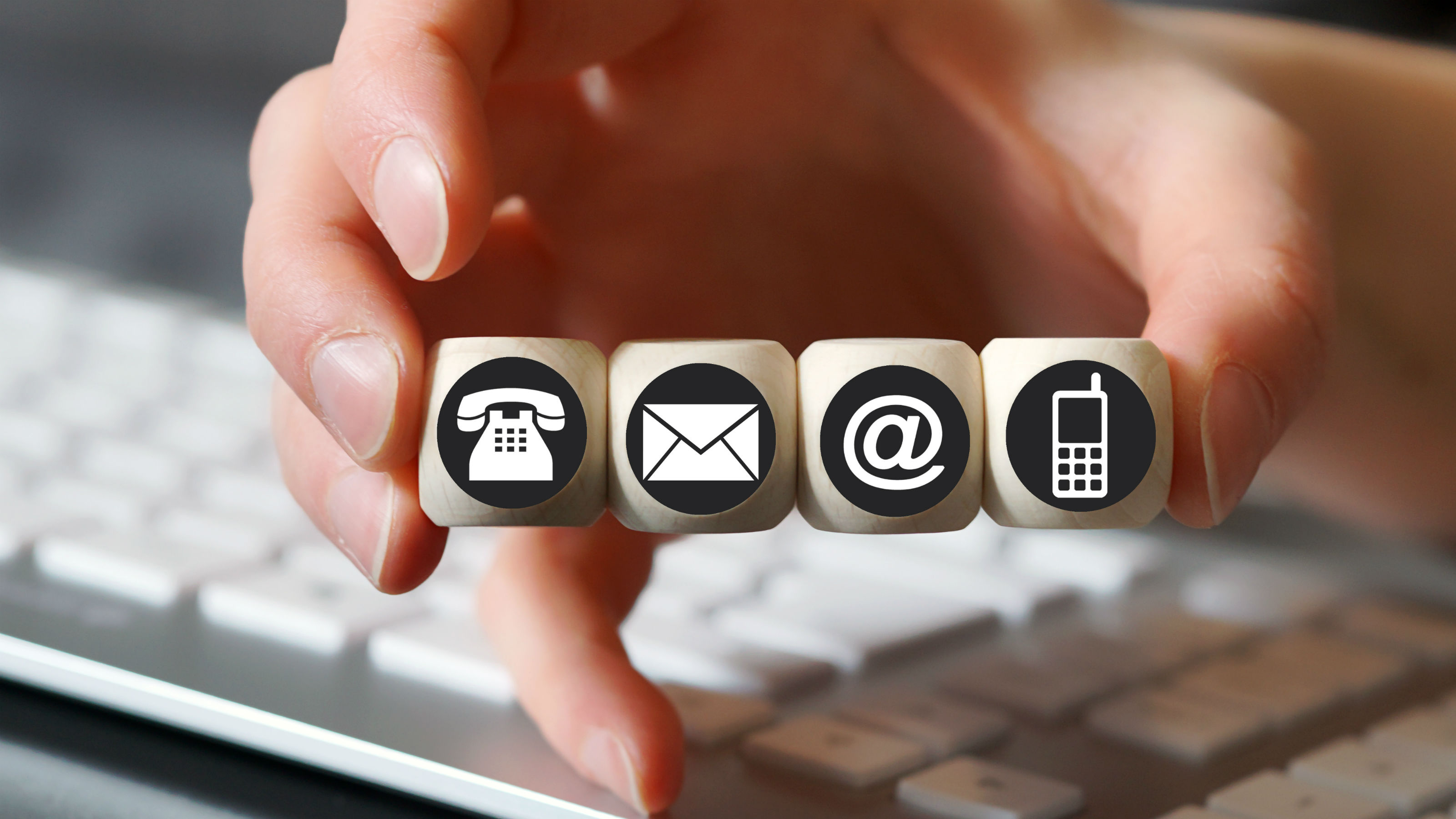 A hand holds four cubes with symbols, a telephone, envelope, at symbol and cell phone.