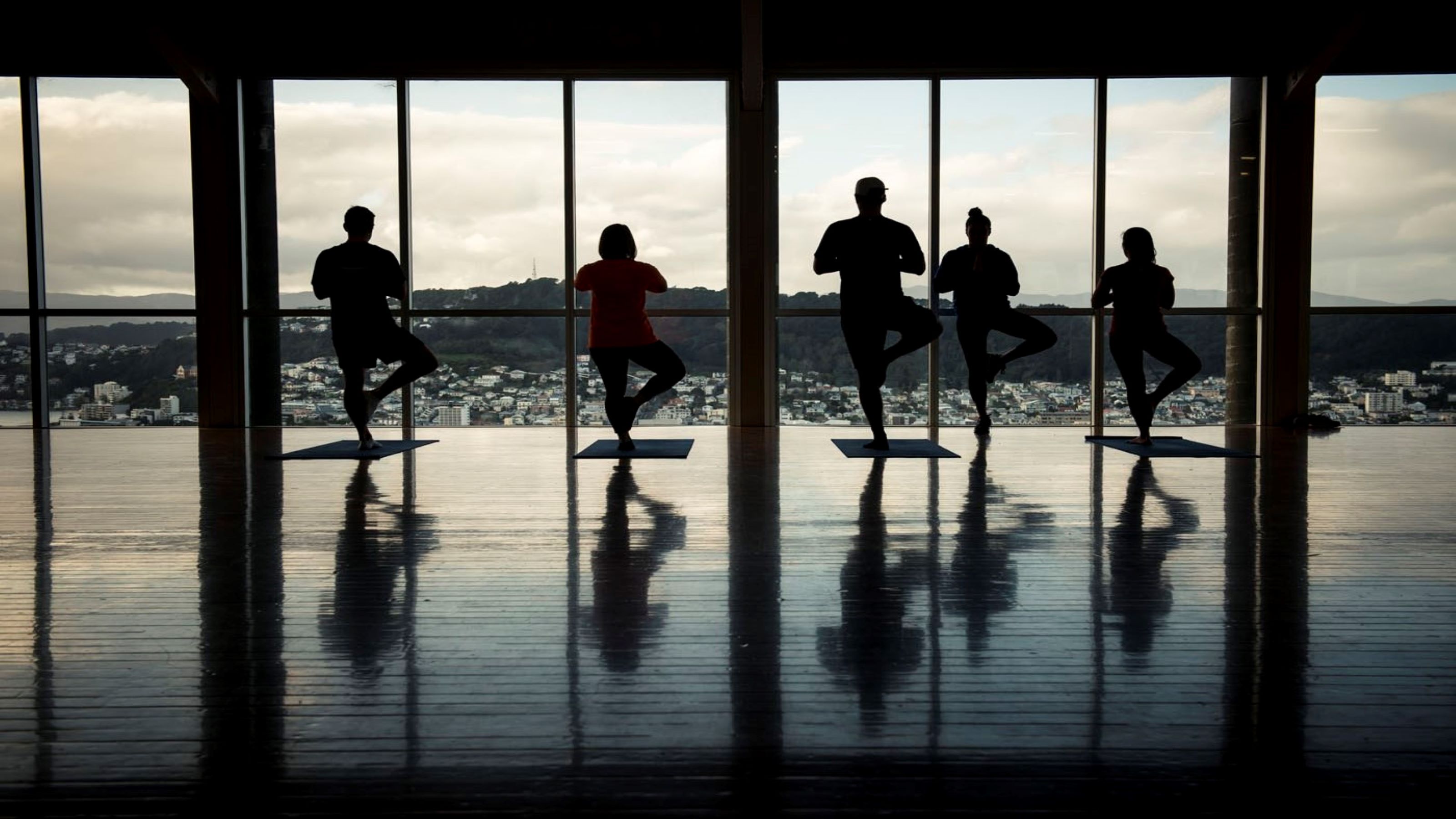 Five people standing in yoga positions in front of window at dusk