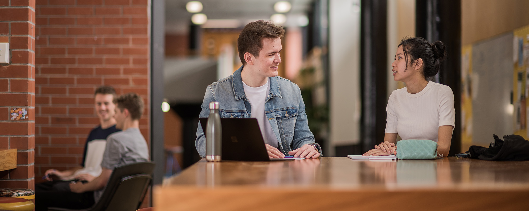 Bachelor of Commerce student Rohan speaks with another student at a table on campus.