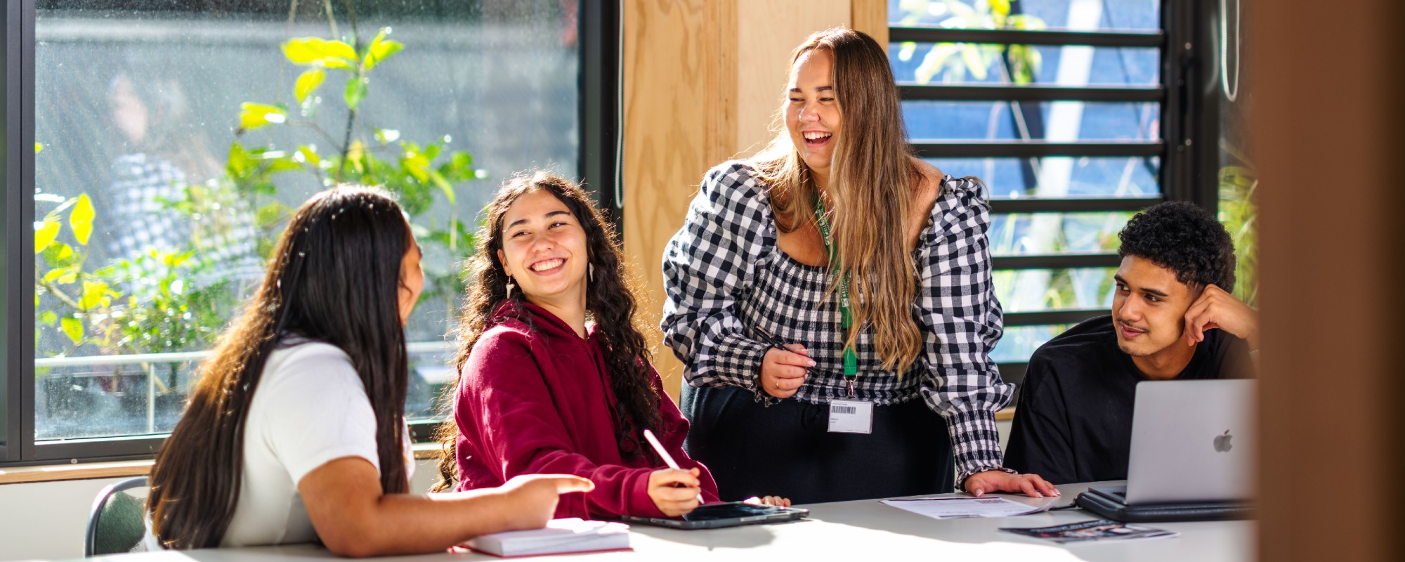 Future students advisor Tayla is standing and smiling at a work table, engaging with three students.