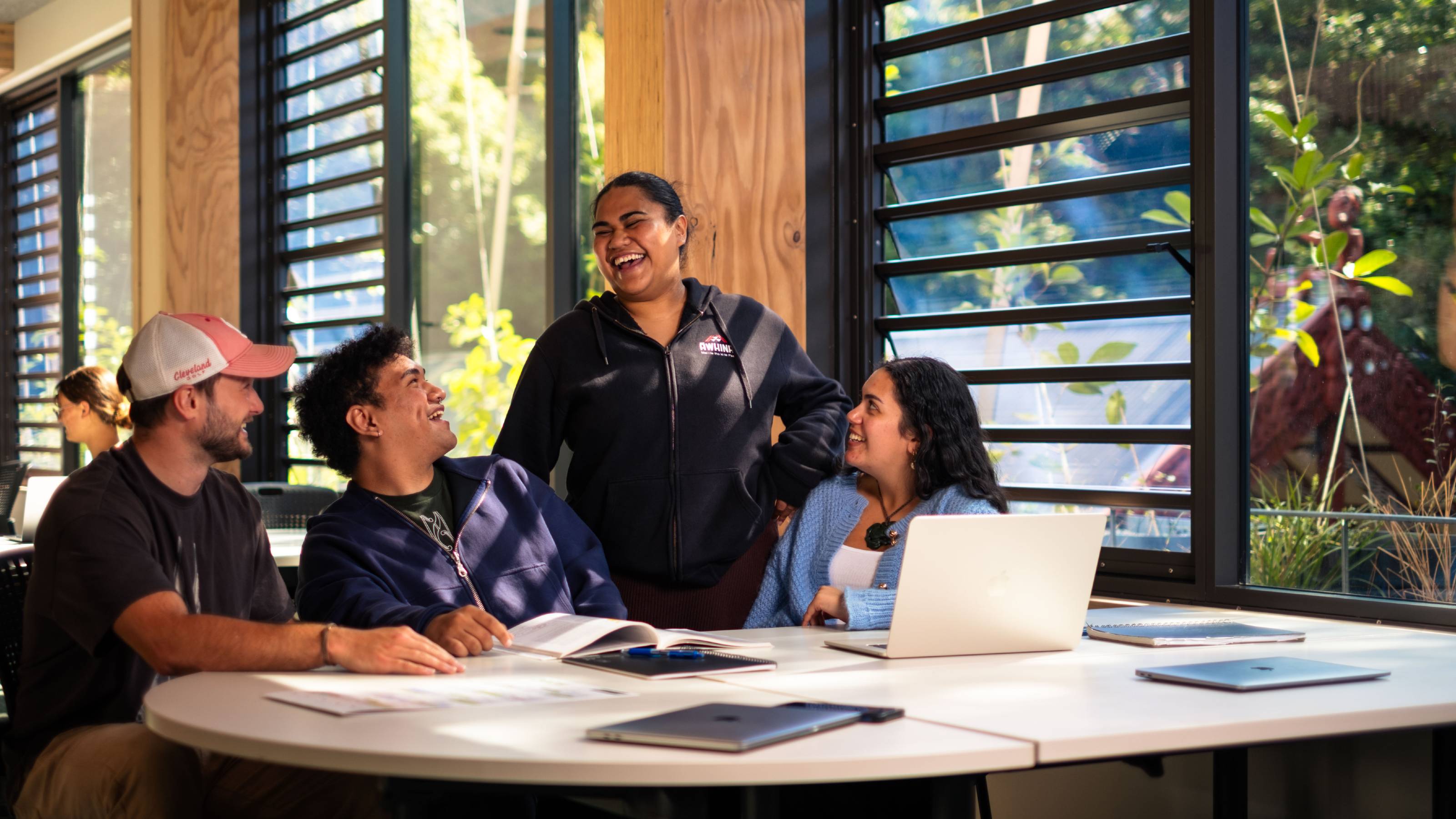 A woman from the Awhina student support team laughing with 3 students seated at a table.