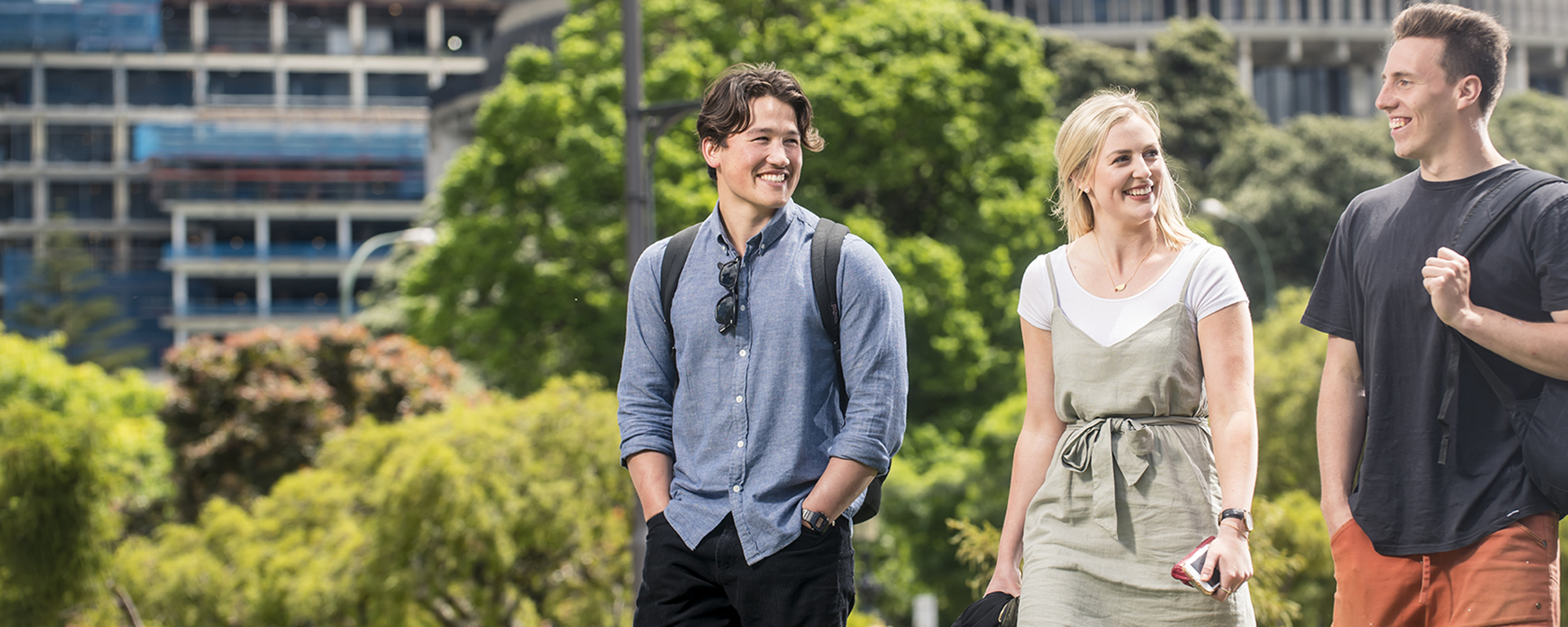 Three students are smiling while walking together across campus.