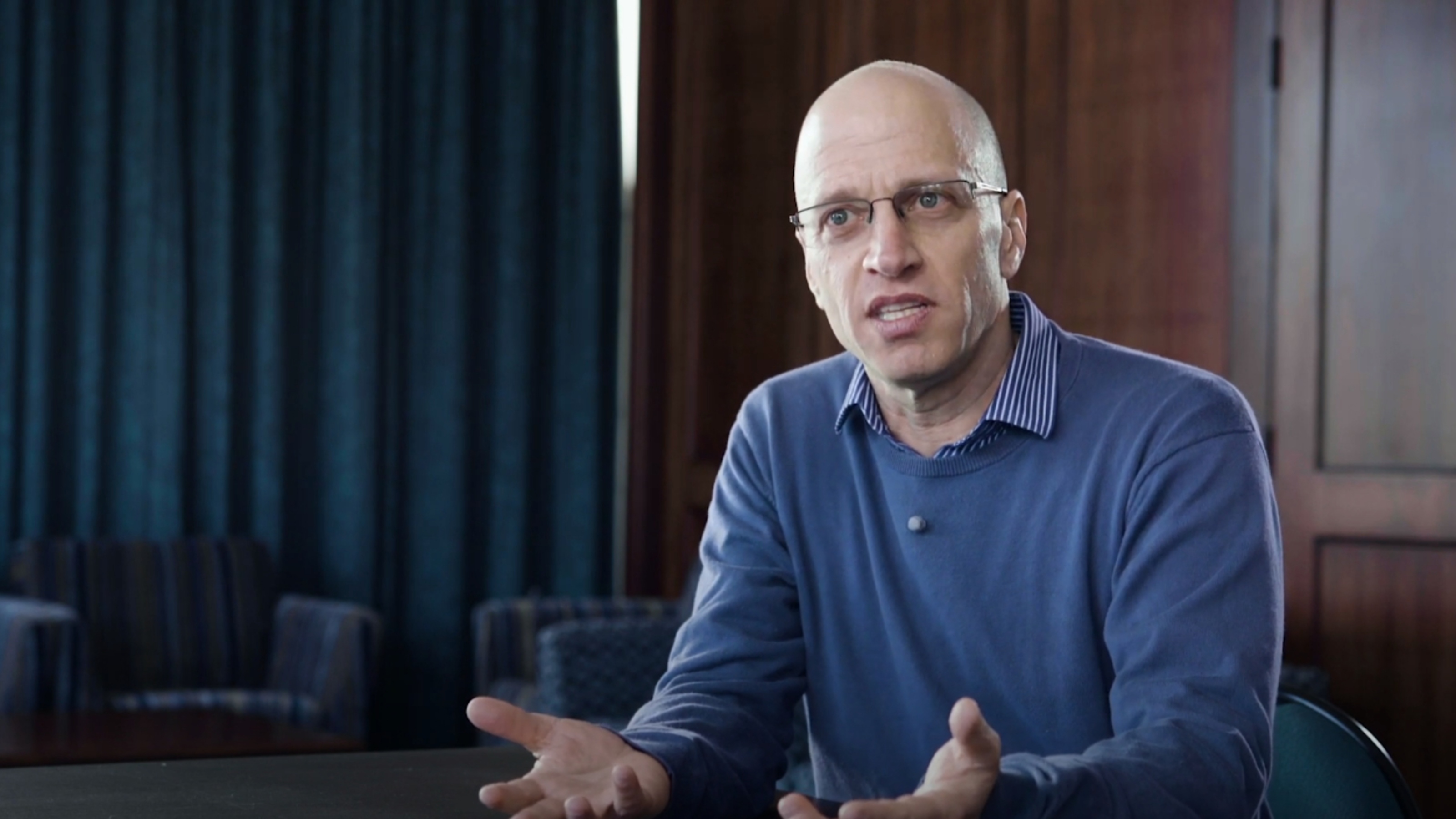 Head and torso of man in blue shirt speaking to someone off camera.