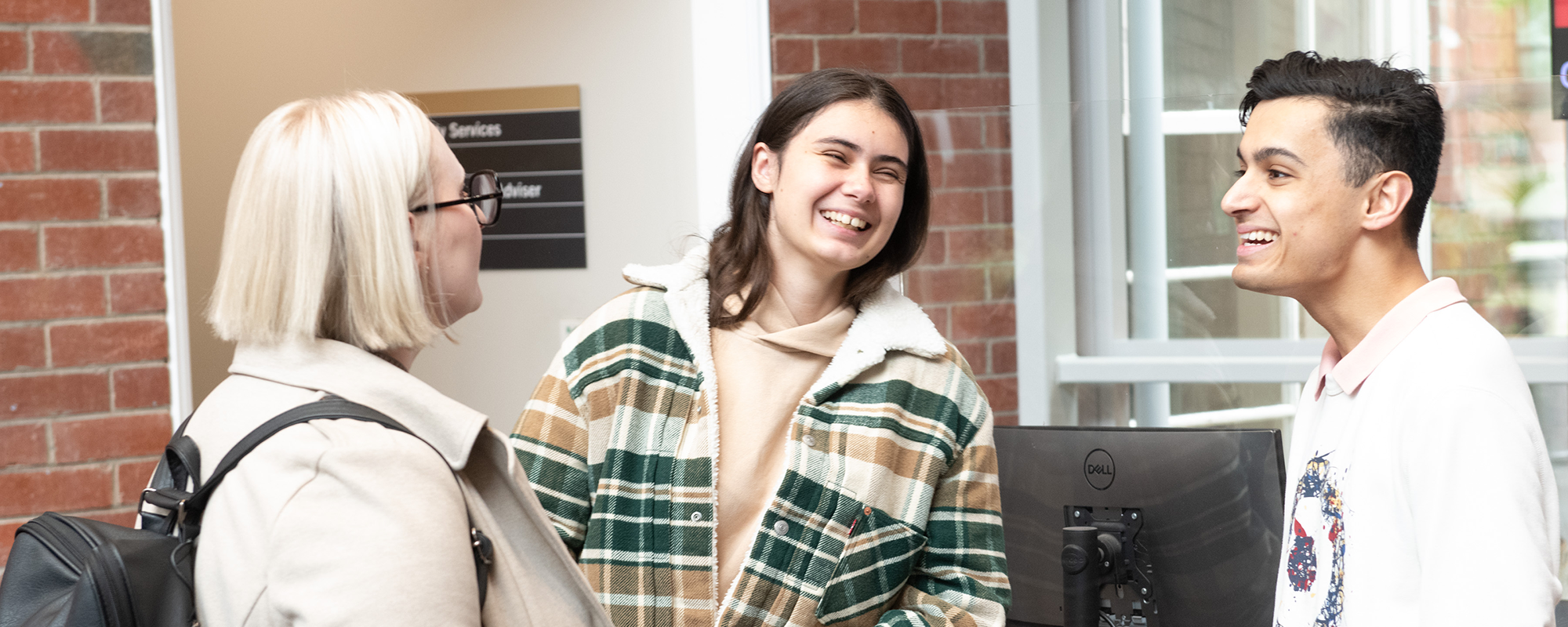 Three students in Hunter building atrium engaged in a conversation.