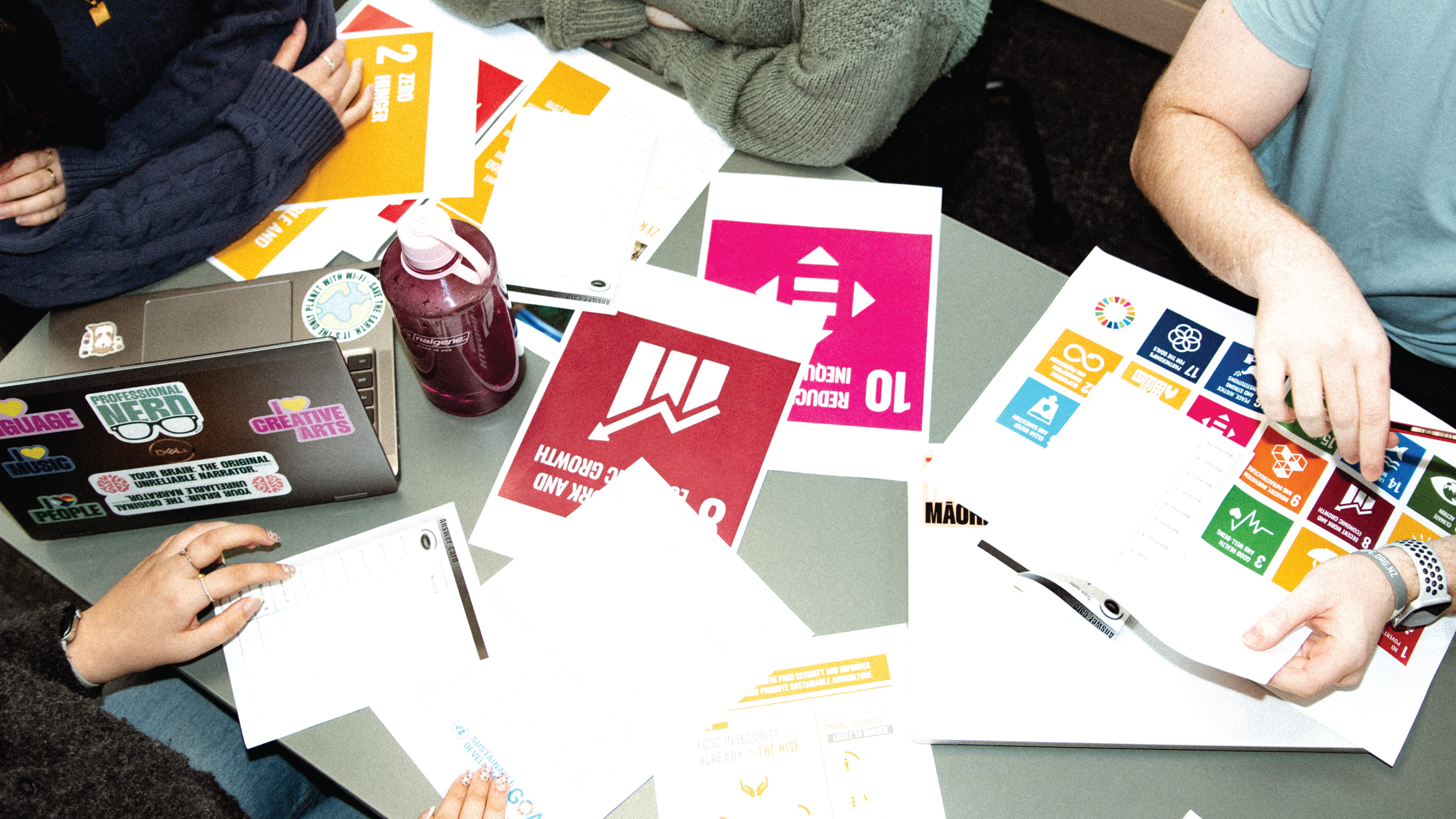 Top-down view of a table covered in various printed pieces of paper, with arms pointing at them.