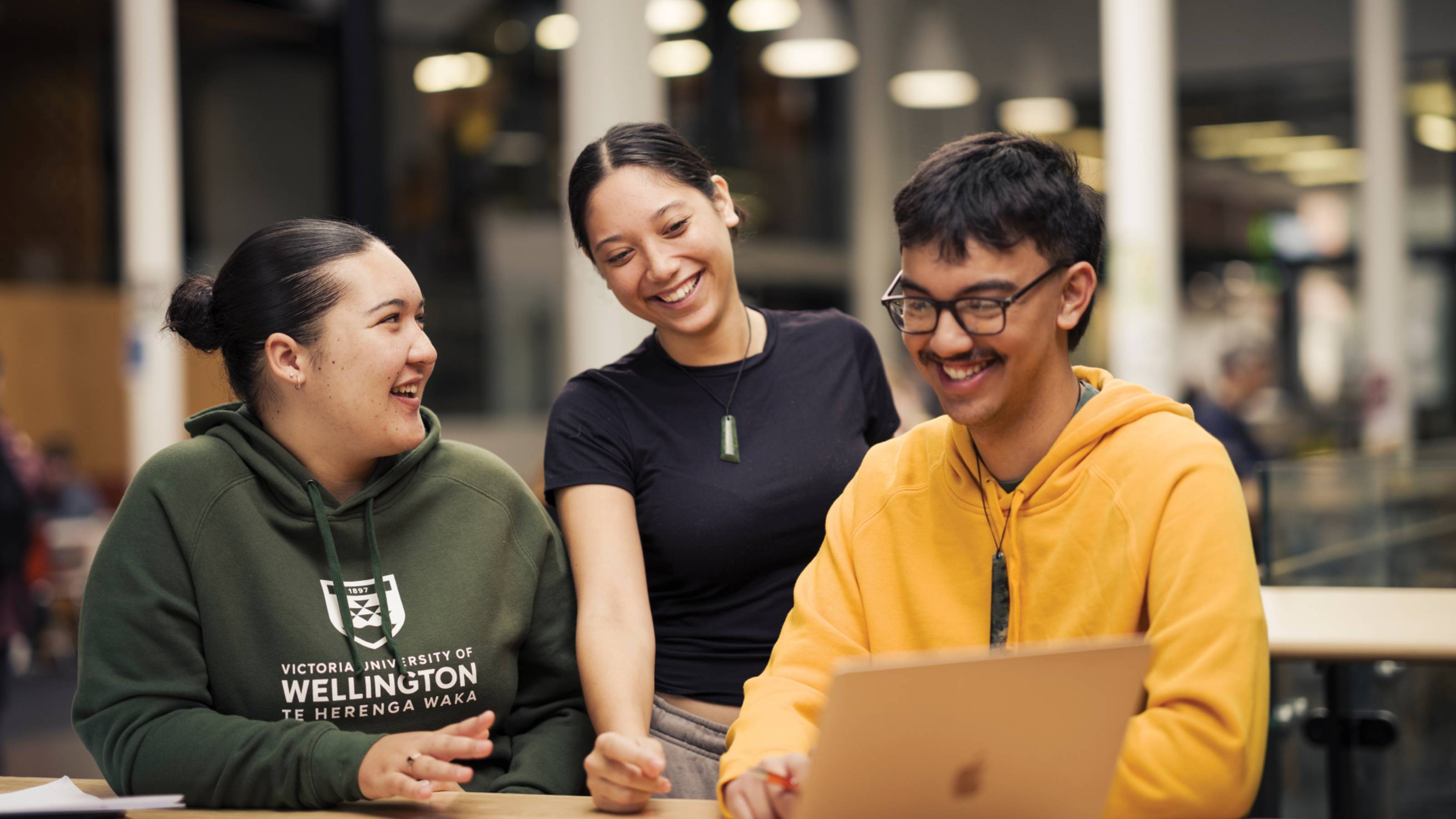 Three Māori students gathered around a laptop