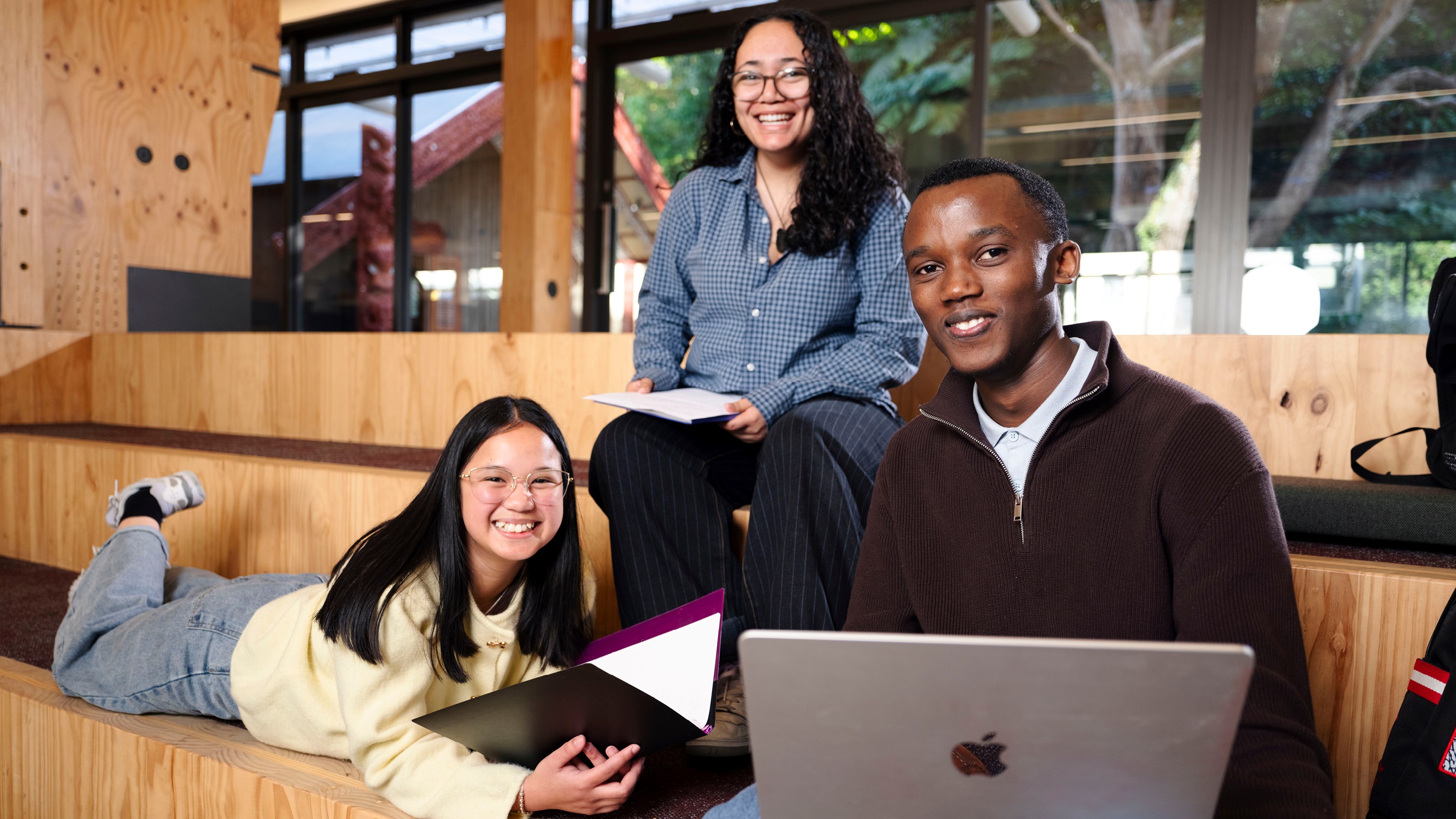 Two girls and a boy are sitting with their laptops on the Kelburn campus