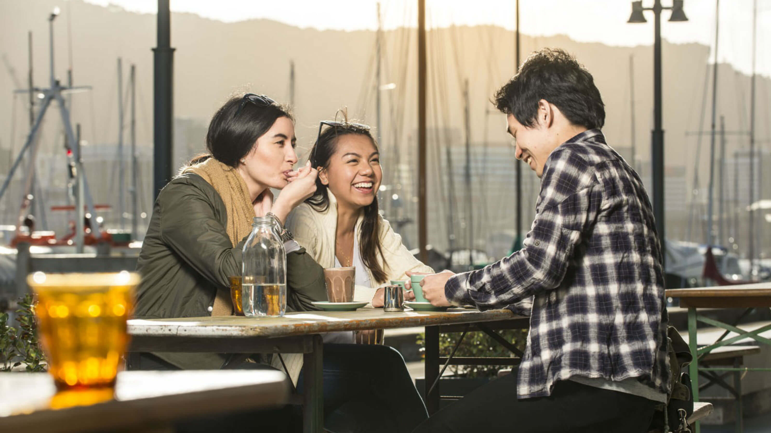 Three friends sitting around drinking coffee on the waterfront.