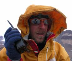 A researcher wears an orange jacket and holds a walkie talkie.