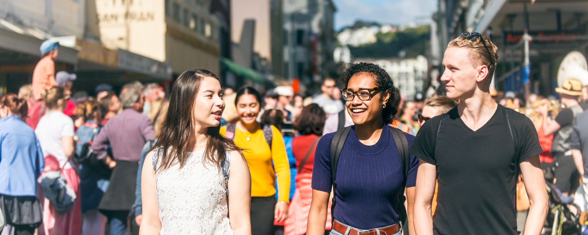 Three university students walking and smiling at a busy street festival.