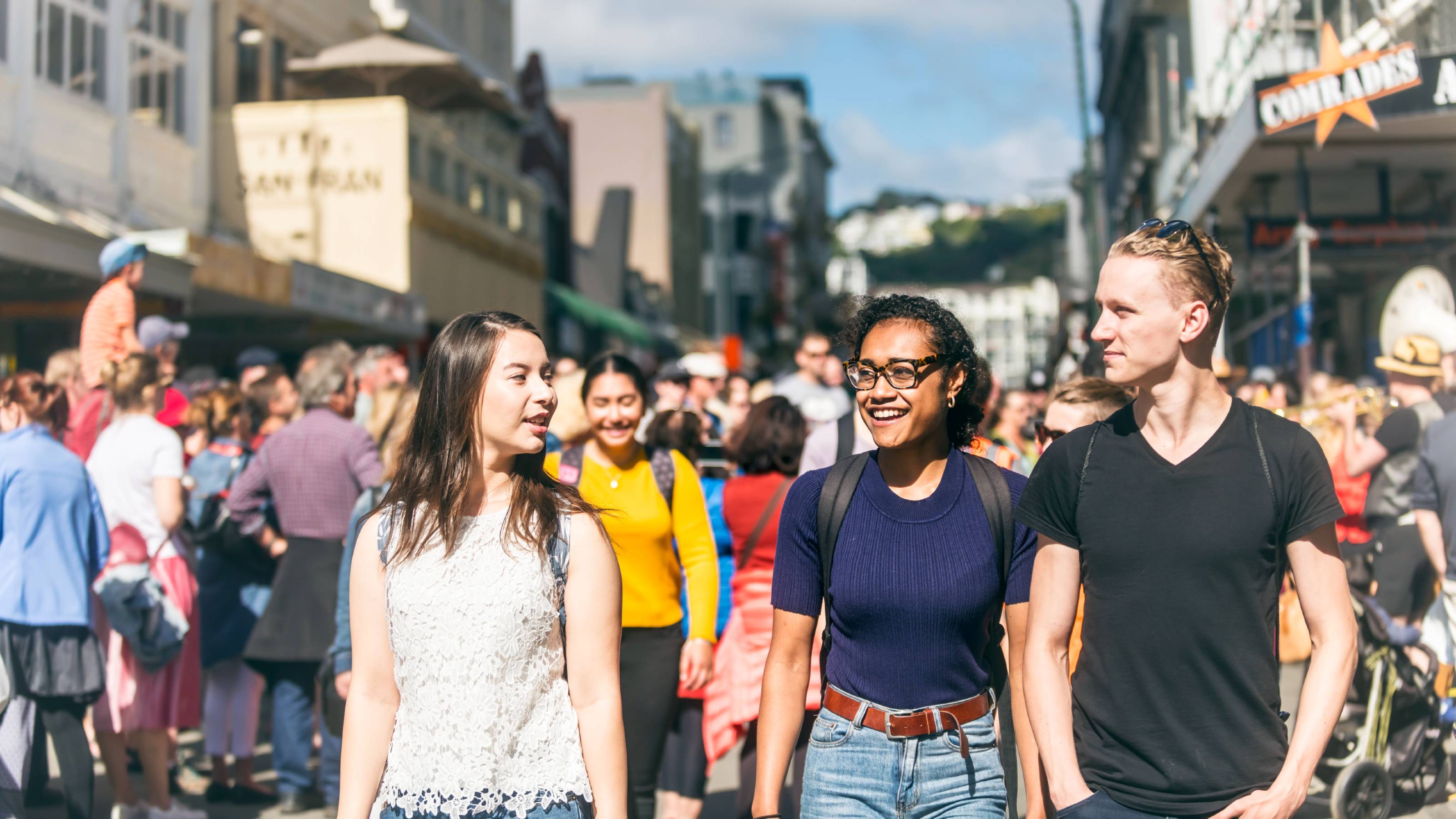 Three university students walking and smiling at a busy street festival.