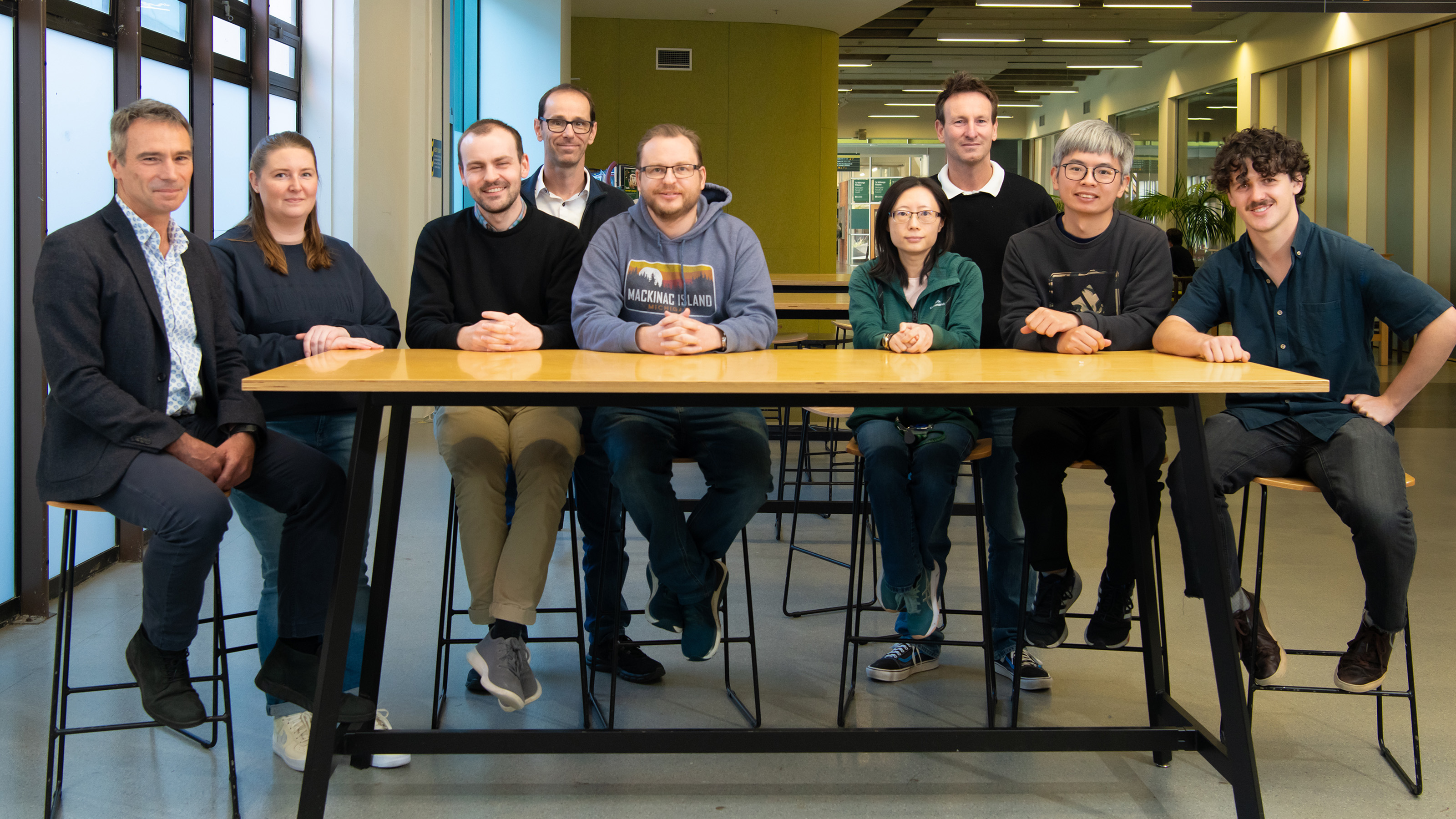A group of nine people sitting and standing around a table.