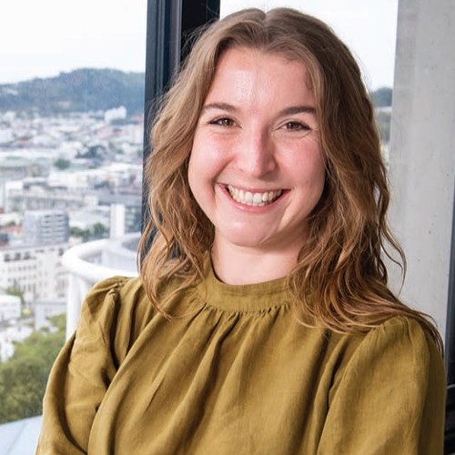 Close up of Jess Shaw standing at a window with the city behind her