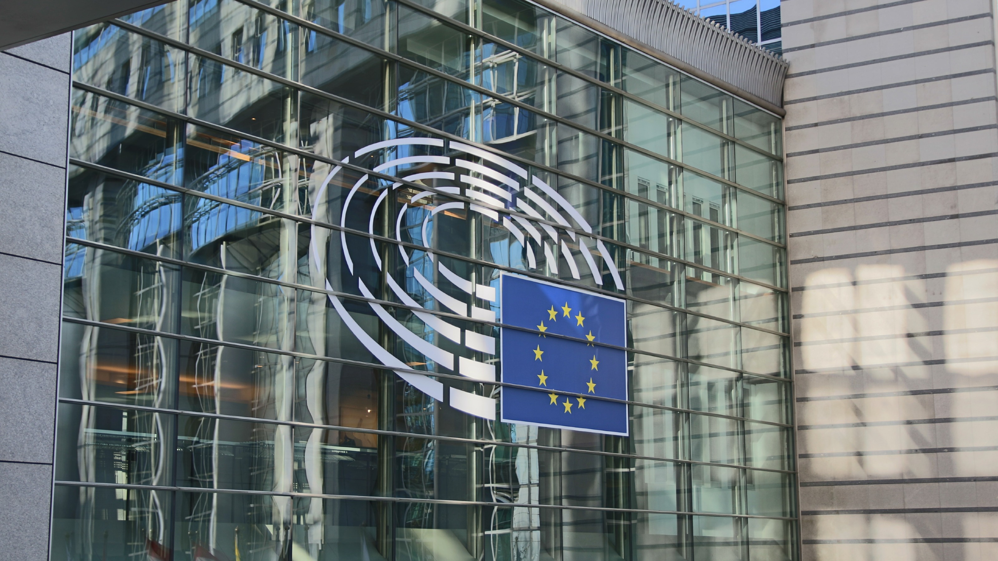 A building facade with a flag displaying on a large wall of glass.