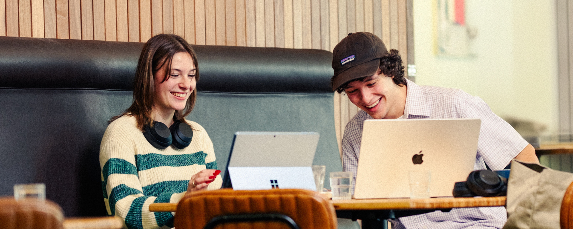 Smiling students sitting at table in campus cafe with laptops.