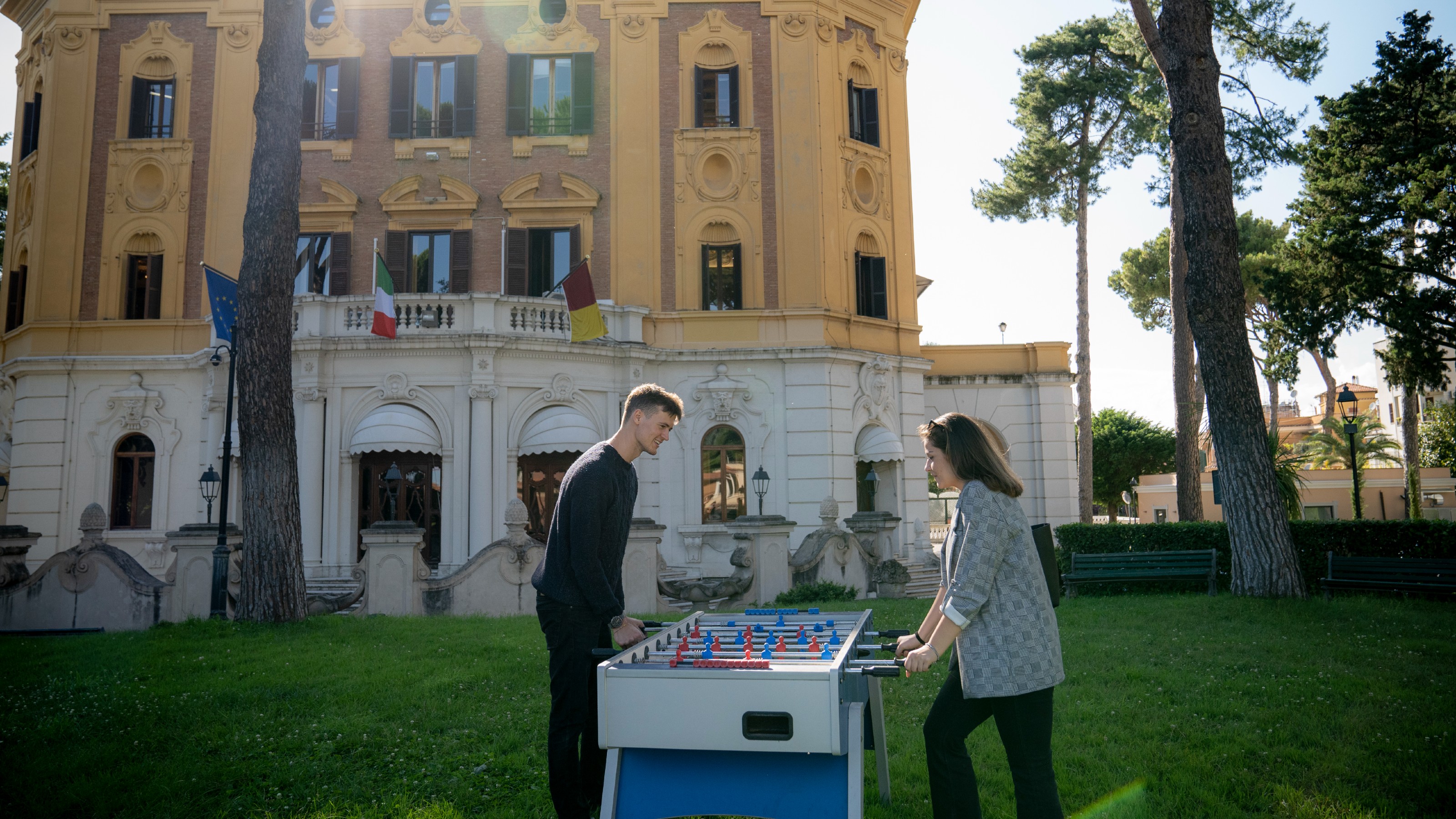 Two students are playing foosball on the lawn outside an old building at LUISS university in Rome.