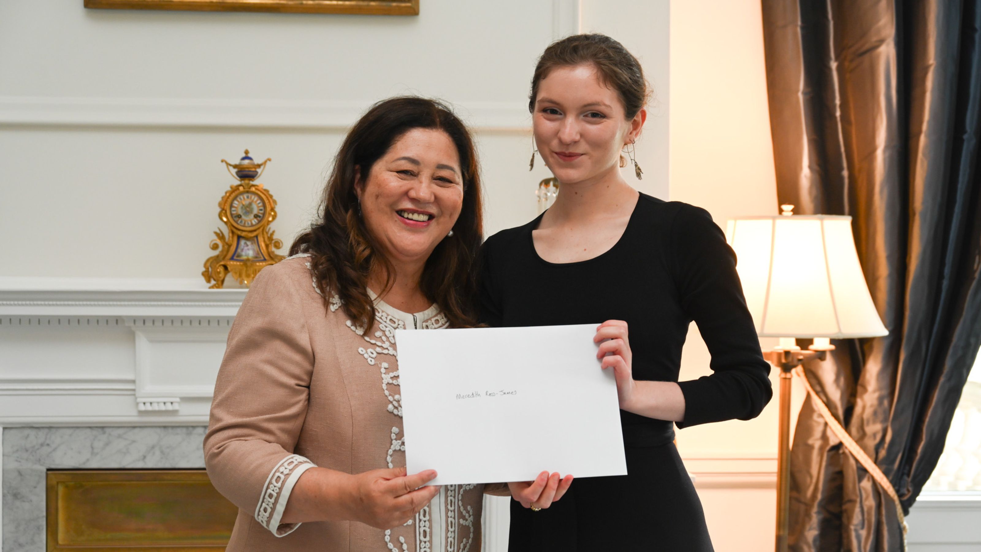 Two women smiling, one handing an envelope to another 
