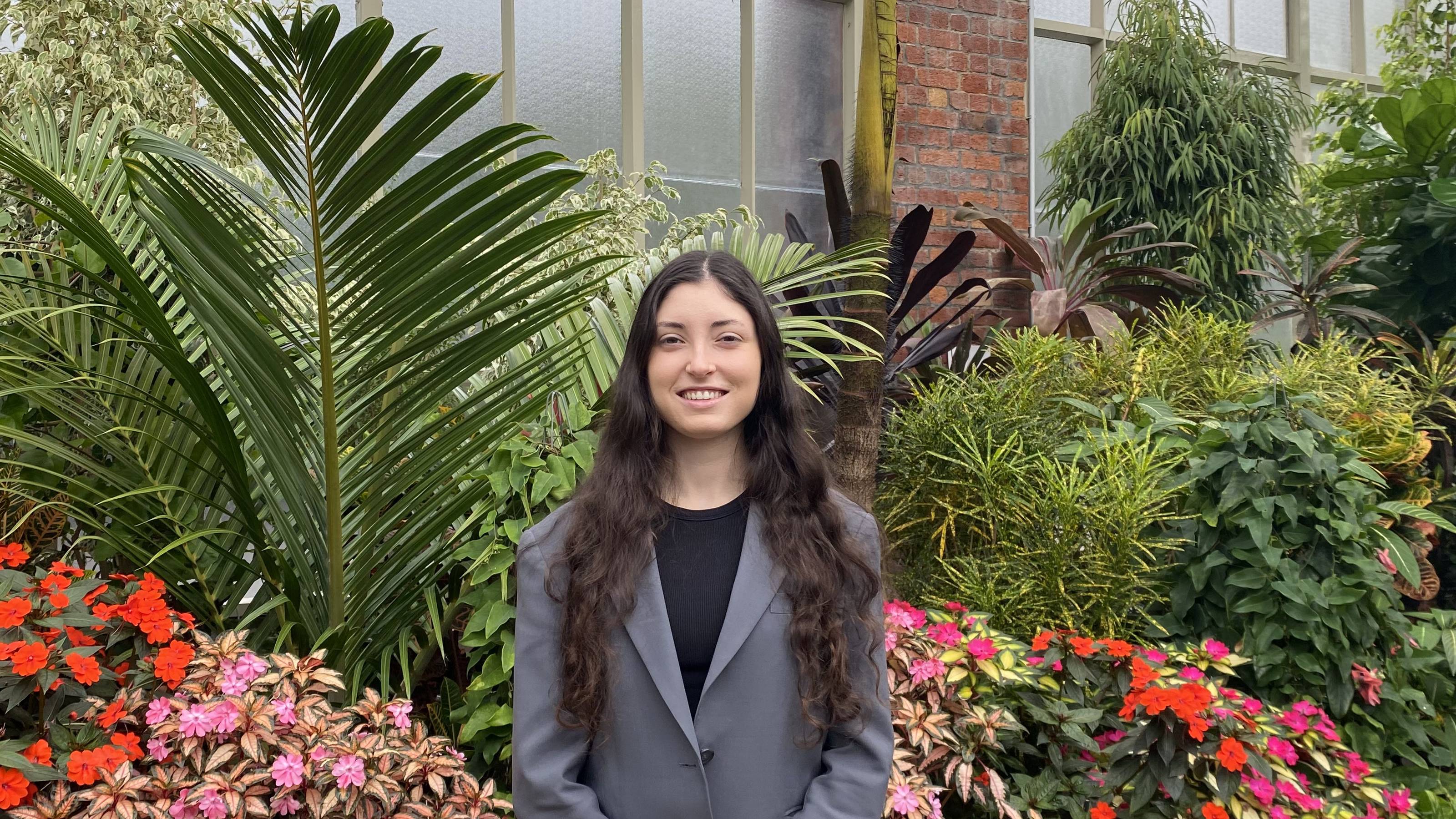 Caitlin Ashby standing in front of some flowers and foliage. 