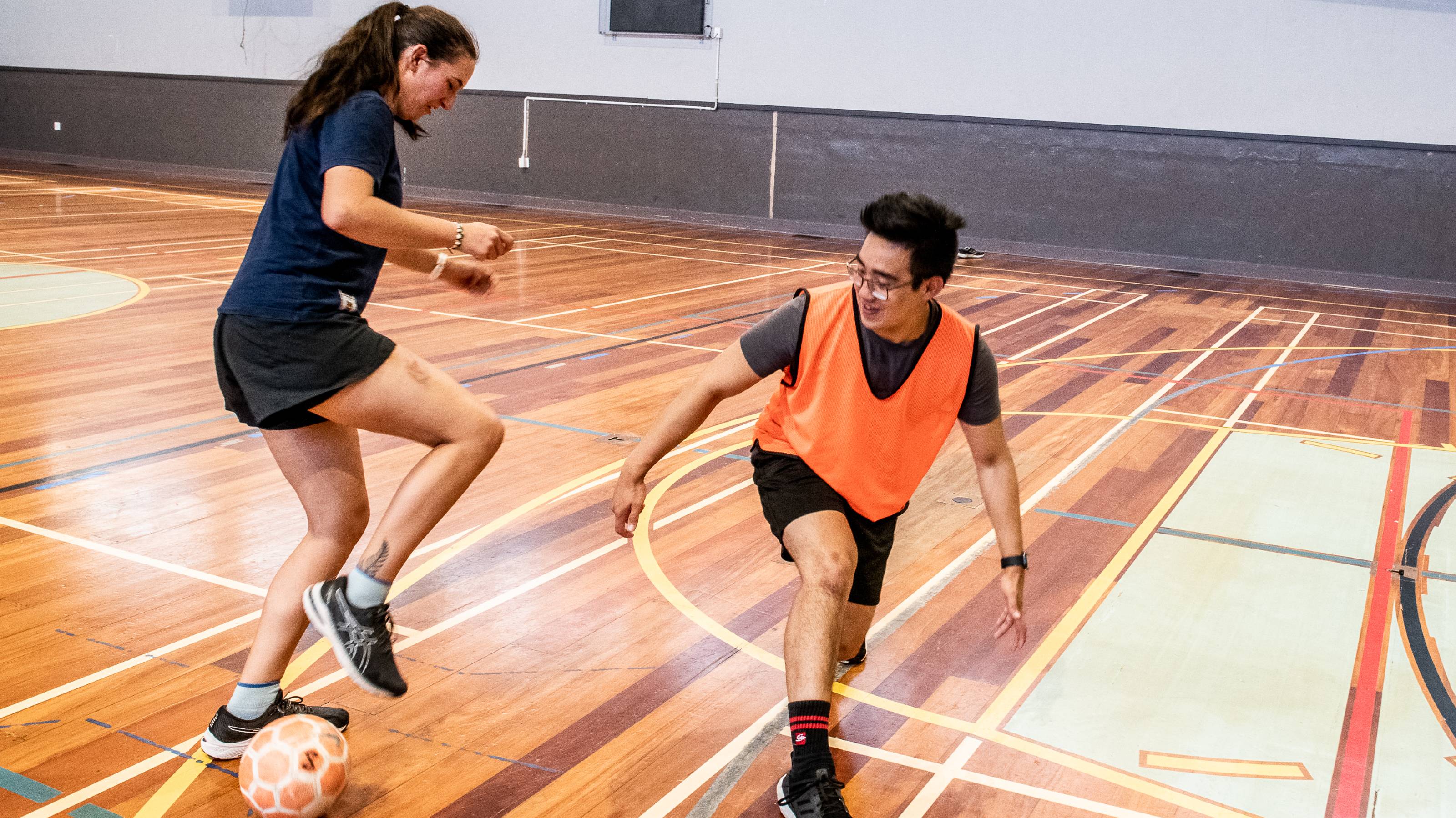A futsal player dressed in black dribbles past a player in orange, deceiving him with fancy footwork