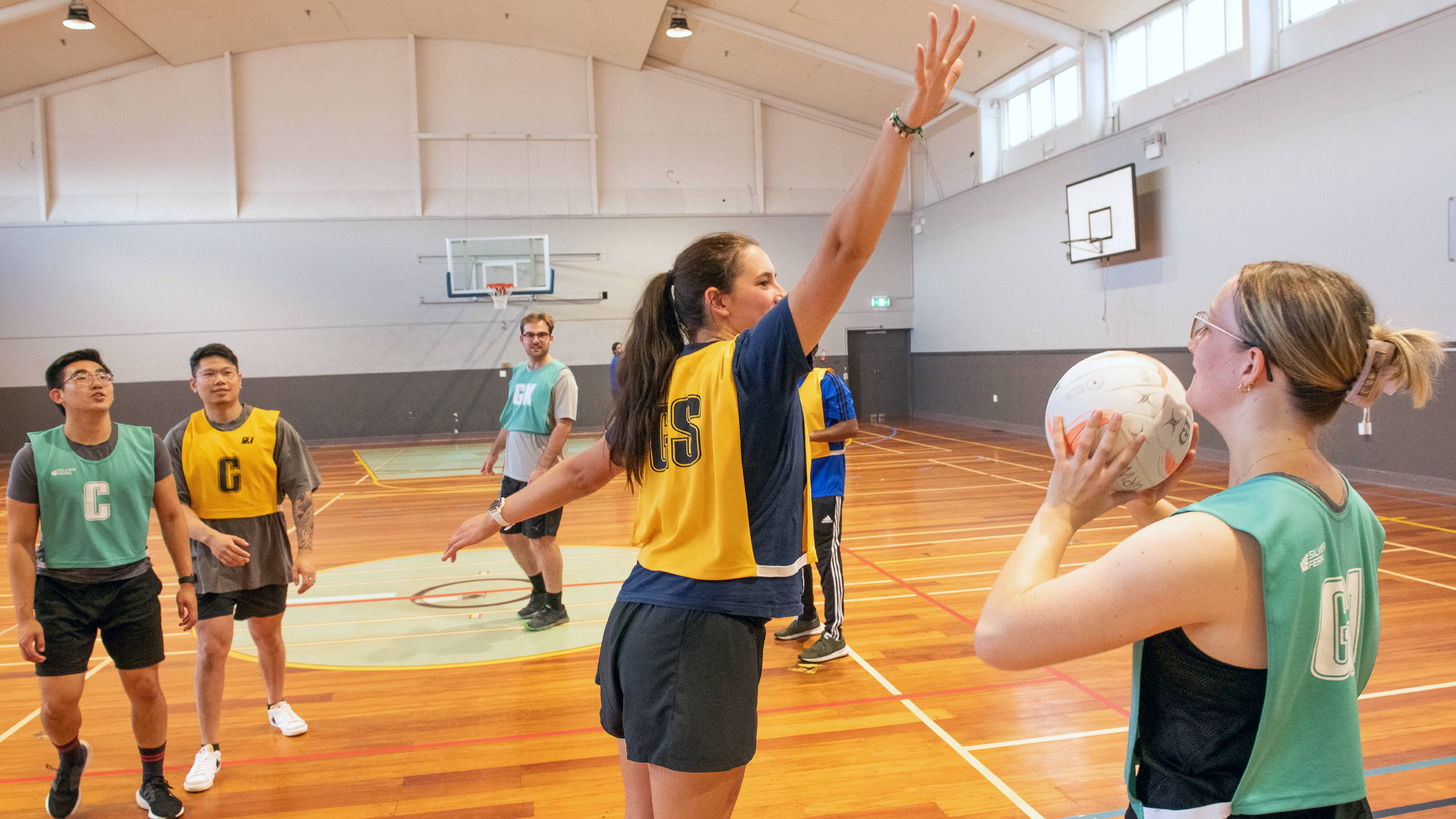 A player in a yellow GS bib stretches out to block a pass from a teal-bibbed player.