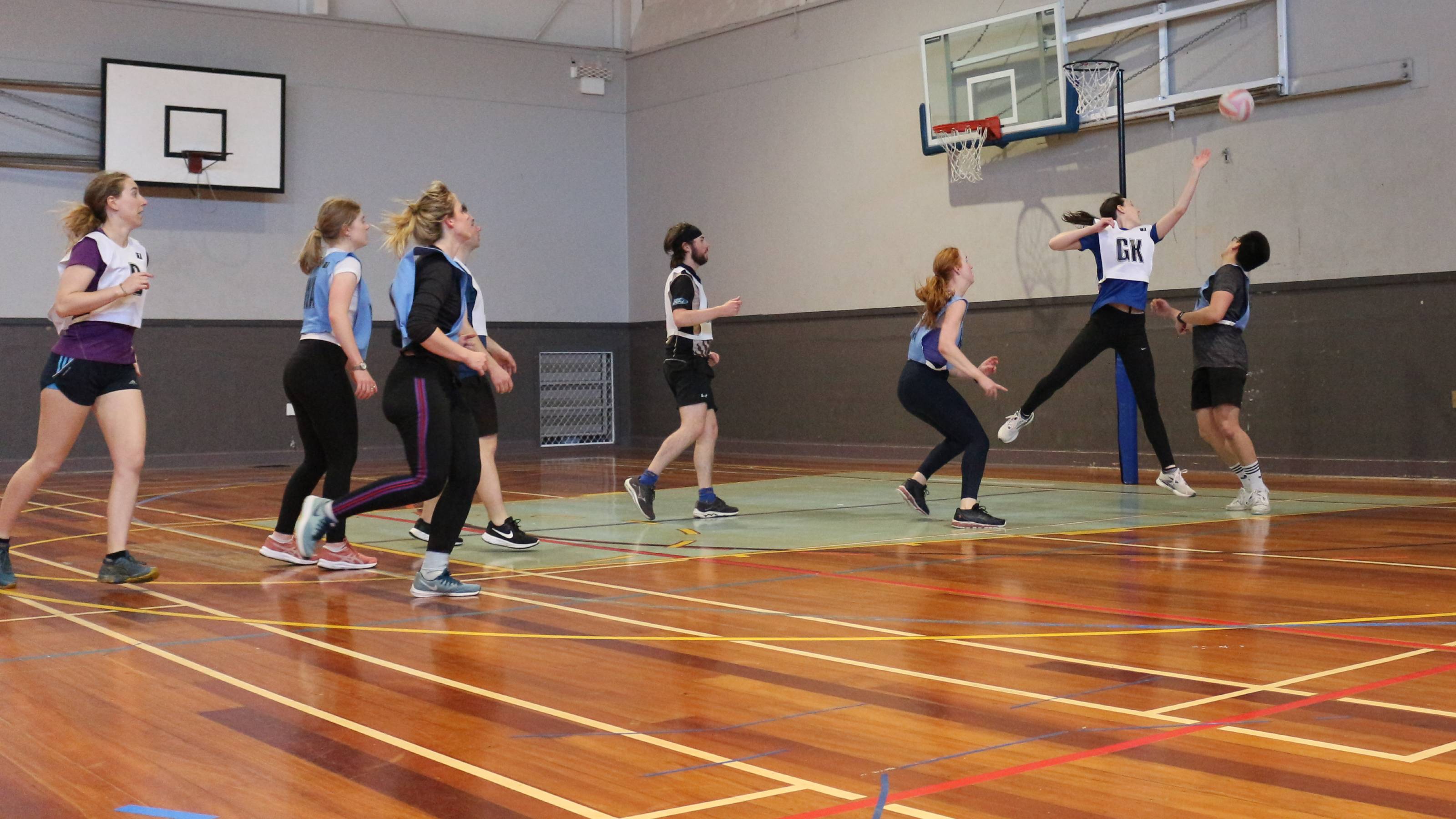 Netball players with a shiny wooden court in the foreground