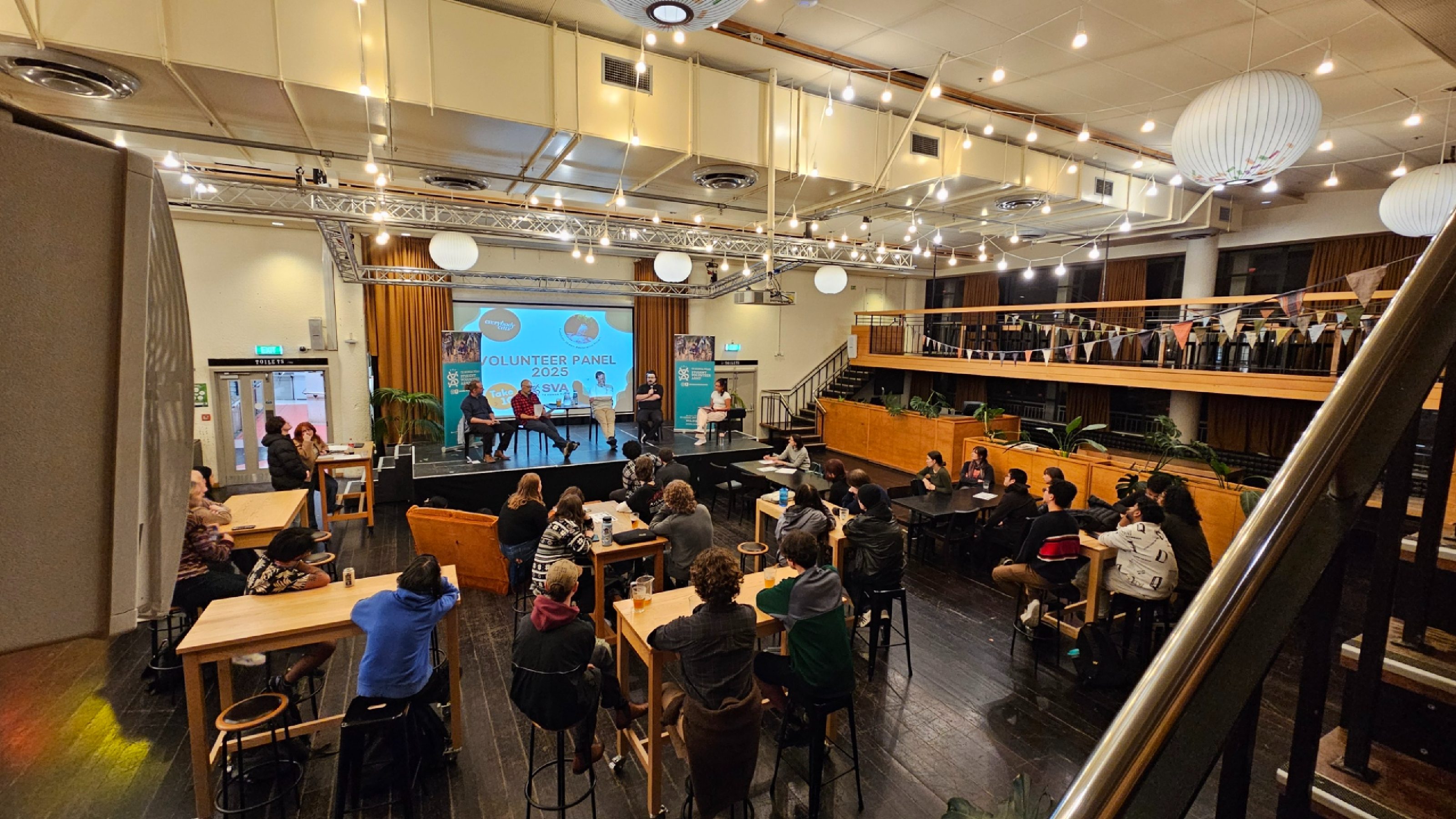 A panel sit on stage and view of the audience watching.