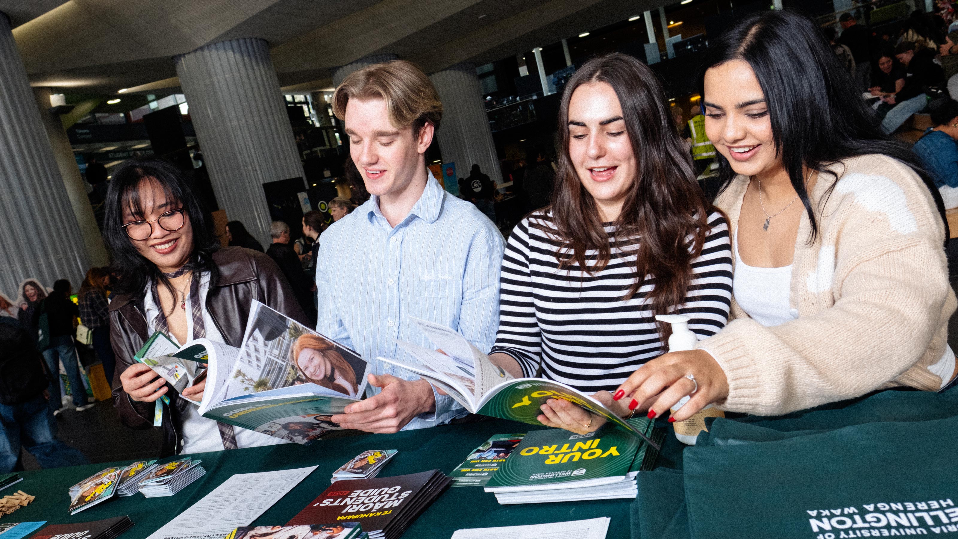 4 students sitting at a table covered in a green cloth reading university leaflets and guides