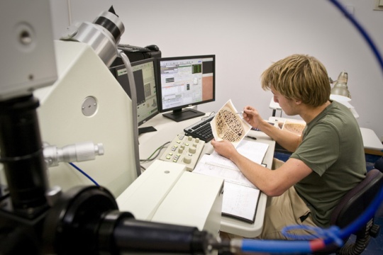 A student inspecting an image at a desk with complex equipment.