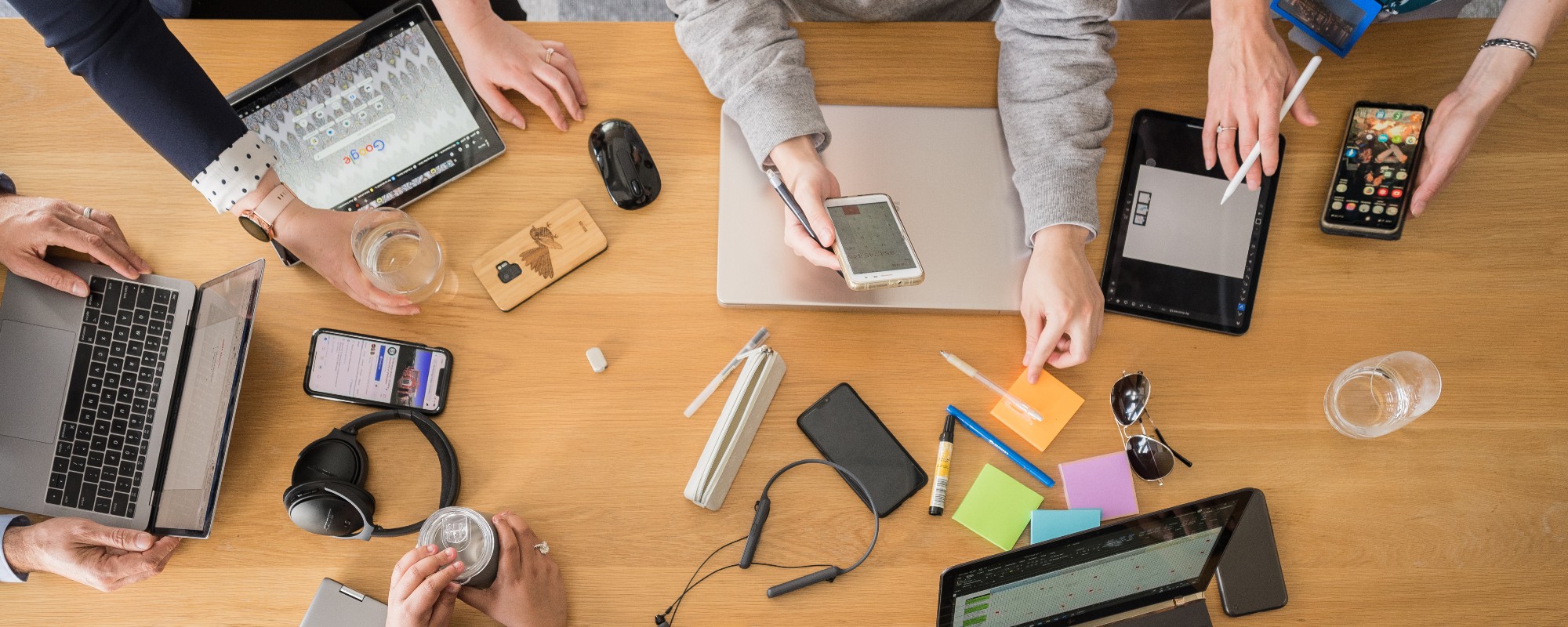 A table covered with colourful stationery, laptops, and peoples' arms.