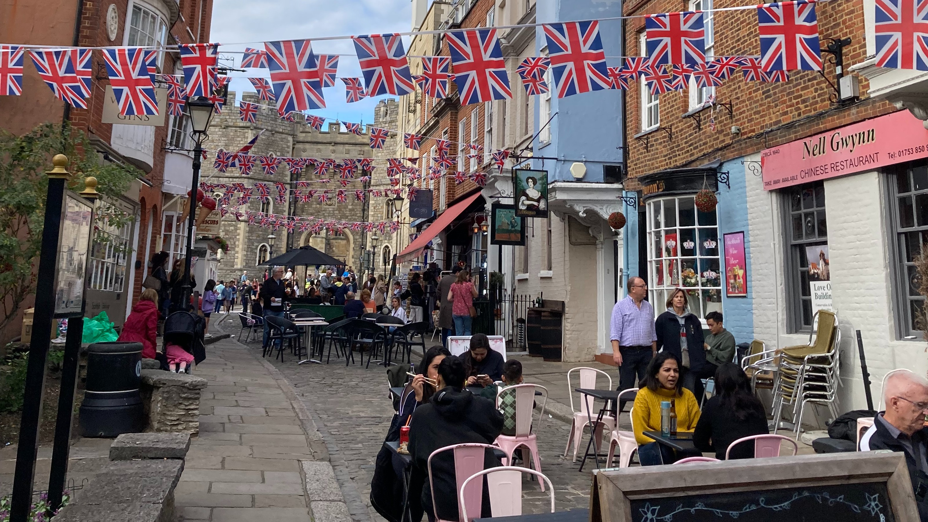 A quaint street near Windsor Castle in the UK, strung with Union Jack bunting, and filled with tables and chairs from nearby restaurants.