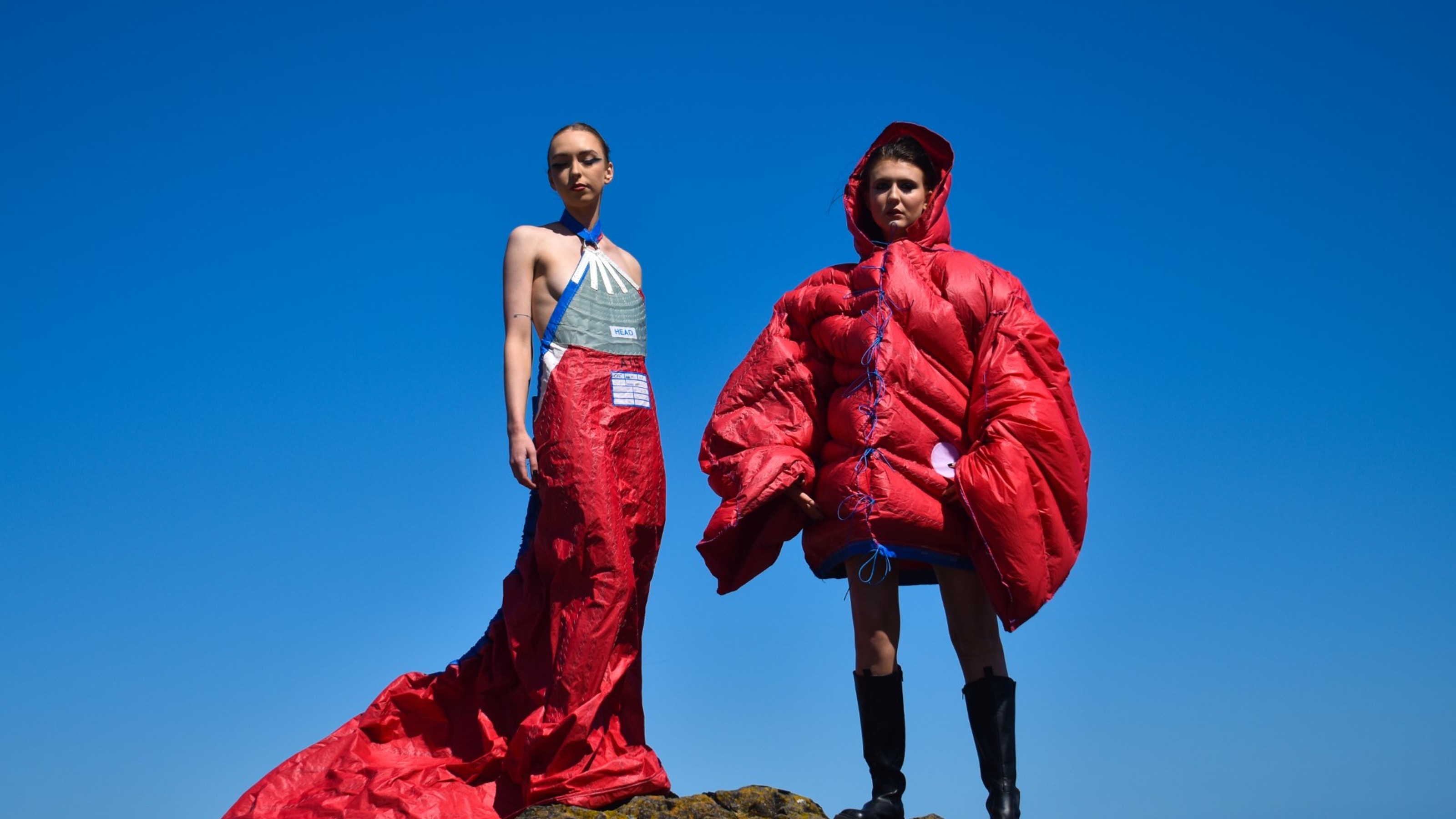 Two models photographed in red garments with blue sky backdrop