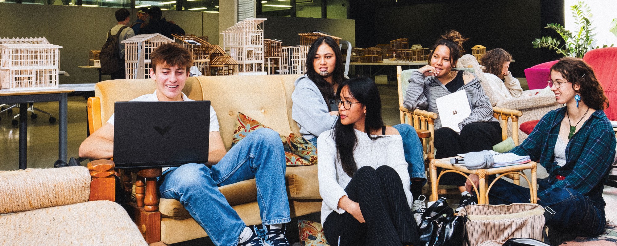 A group of FADI students sitting around smiling, architecture mock ups in the background